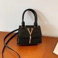 Mini-Handtasche in Schwarz mit goldener V-Verzierung und Fransen auf Holzgrund - Schwarz