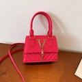 Pinke gesteppte Handtasche mit goldenem V-Logo und Quaste auf einem Holztisch - Rosarot
