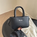 Minimalist black leather handbag with silver logo on a table, 2-way carry style - Black