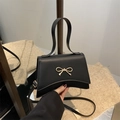 Elegant black crossbody bag with gold bow clasp and stylish curved trapezoid shape - Black
