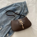 Bolso de hombro marrón mate minimalista con borla dorada sobre un fondo de tela vaquera - Marrón