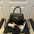 Minimalist black leather crossbody bag featuring a golden bow buckle and round top handle - Black