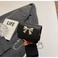 Detail of a black leather mini crossbody bag featuring a silver bow buckle and chain strap - Black