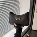 Matte black leather shoulder bag with a gold metal bow clasp and minimalist curved design - Black