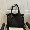 Minimalist black nylon tote bag with tennis racket charm and woven cord on a modern chair - Black