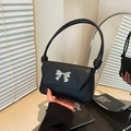 Minimalist black leather underarm bag with silver butterfly buckle on an elegant desk - Black