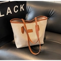 Dettaglio della borsa tote in tela con manici in pelle marrone e toppa sul divano - Marrone Scuro
