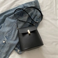 Minimalist black matte leather crossbody bag with elegant gold metal buckle on denim jacket - Black