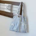 Light blue tote bag with white flower embroidery and a lace bow on a wooden rack - Blue
