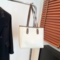 Bolso tote minimalista crema con ribete marrón y anillas metálicas doradas colgado - Blanco Roto