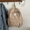 Minimalistischer beiger Nylon-Rucksack mit Smiley-Aufnäher an einem Holzhaken - Khaki