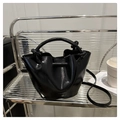 Detail of a black glossy bucket bag with metal ring handle on a modern shelf - Black