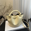 Chic pale yellow bucket bag with knotted handle and shoulder strap on a white book - Yellow