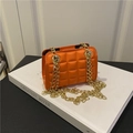 Orange gesteppte Schultertasche mit doppelten Goldketten auf weißem Deko-Buch - Orange