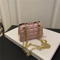 Rosafarbene gesteppte Umhängetasche mit goldener Kette auf einem weißen Buch - Rosa