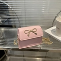 Pink mini crossbody bag with a golden bow buckle and fine chain strap in a lifestyle setting - Pink