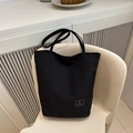 Close-up of a minimalist black tote bag with logo patch resting on a modern white chair - Black