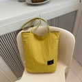 Macro detail of yellow pleated fabric tote bag featuring a black woven logo tag - Yellow