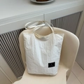Minimalist white tote bag with pleated texture and black brand patch on casual chair - White