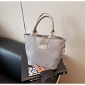 Detail of grey nylon handbag showing the fashion label and metallic champagne gold handles - Light Gray