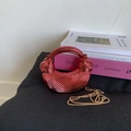 Détail d'un sac lune rouge métallique avec texture ondulée et poignée ronde sur livres - Rouge