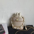 Detail of woven straw bucket bag featuring pearl accent and gold chain shoulder strap - Beige