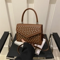 Bolso bandolera de cuero marrón con tachuelas plateadas y asa sobre un libro - Marrón