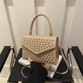 Bolso bandolera beige con tachuelas plateadas y asa de mano en una silla negra - Caqui