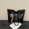 Grand cabas noir avec breloque ours et cordon tressé posé sur un banc en cuir - Avec Pendentif / Noir