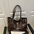 Deep brown large tote bag in glossy leather finish with metal buckle detailing on black chair - Coffee