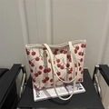 Minimalist white tote bag with red cherry prints and dual handles on a chair - White