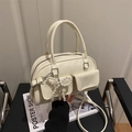 Creamy white crossbody bag with twin pockets and a pearl bow charm on a leather chair - White