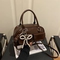 Dark brown faux leather crossbody bag with a white pearl bow charm on a chair - Brown