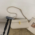 Detalle de un bolso de hombro de cuero beige con hebilla dorada sobre un taburete tejido - Blanco