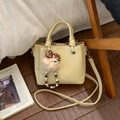 Gros plan du sac à main en cuir beige avec breloque ours en peluche et bandoulière - Avec Pendentif / Jaune