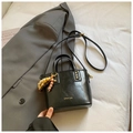 Sac seau noir brillant avec breloque en perles et logo doré sur fond de veste grise - Noir