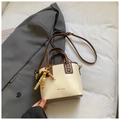Détail d'un sac seau crème minimaliste avec garniture en cuir marron et breloque vintage - Blanc Cassé