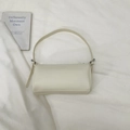 Close-up of cream lychee leather texture and metal buckle on minimalist shoulder bag - White