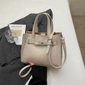 Schicke beige Tragetasche aus Kunstleder mit Drehverschluss auf grauem Blazer - Beigegrau