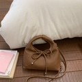 Brown leather handbag detail featuring a decorative bow and textured lychee pattern leather - Brown