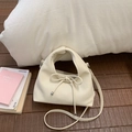 Dettaglio di una borsa in morbida pelle color crema con fiocco su pavimento in legno scuro - Bianco