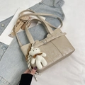 Chic beige bucket bag with leather strap and plush bear charm on denim background - Khaki