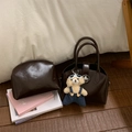 Close-up of dark brown glossy handbag set with teddy bear charm on wood floor - Brown