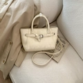 Dettaglio borsa a mano in ecopelle crema con fibbia su un divano in tweed e trench - Bianco Sporco