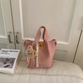 Borsa a secchiello rosa con trama a grana e ciondolo a orso su un divano morbido - Rosa con ciondolo