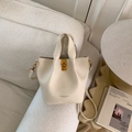 Close-up of beige lychee grain leather bucket bag with turn-lock and removable strap - No Pendant / White