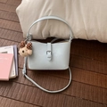 Light blue bucket bag with leather texture and cute bear charm in a lifestyle setting - With Pendant / Blue
