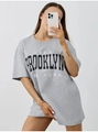 Dettaglio della stampa Brooklyn e del taglio a spalla bassa sulla t-shirt grigia - S / Grigio chiaro