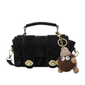 Bolso de mano negro con textura, herrajes dorados y un colgante de monstruo de peluche - Negro