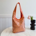 Sac hobo orange avec clous argentés sur une table en marbre blanc - Orange